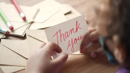 child hand holding thank you letter on table 