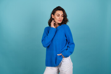 Woman in a blue knitted sweater and natural make-up, curly short hair, looks down thoughtfully to the side