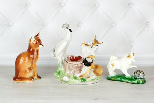 Collection of three porcelain figurines - a fox sitting, a fox and a crane having lunch, a dog playing with a hedgehog