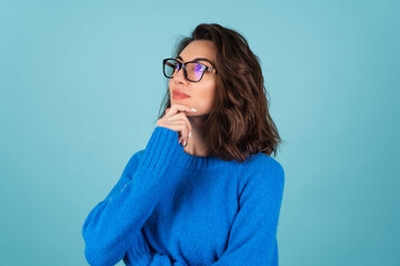 A woman in a blue knitted sweater and natural make-up, curly short hair, glasses on her eyes, looks thoughtfully to the side, meditating - obrazy, fototapety, plakaty