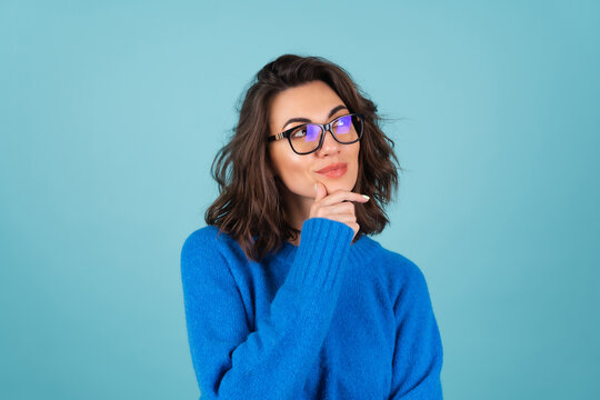A woman in a blue knitted sweater and natural make-up, curly short hair, glasses on her eyes, looks thoughtfully to the side, meditating