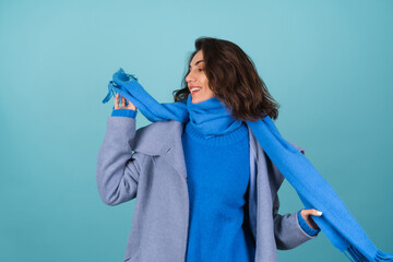 Spring autumn portrait of a woman in a blue knitted sweater, scarf and gray coat, posing cheerfully, smiling, in anticipation of spring