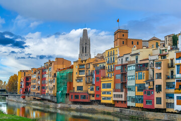 Fototapeta premium Multicolored colorful buildings of Girona Old Town on the embankment of Onyar river, Spain. Fairy-tale landscape of a Spanish town with the tower of Collegiate Church of St. Felix against the blue sky