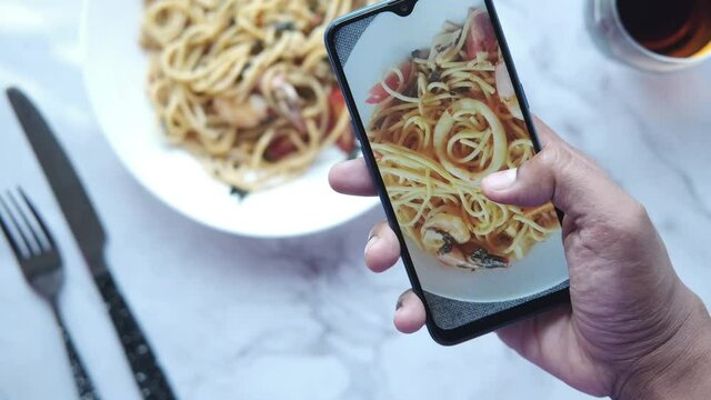 taking picture of plate of sea food pasta with smart phone 