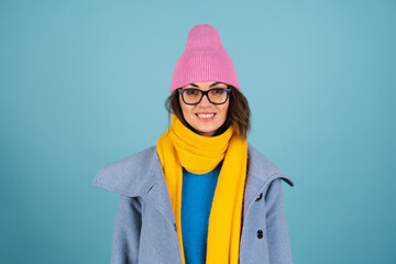 Spring autumn portrait of a woman in a blue knitted sweater, glasses, a yellow bright scarf and a gray coat, smiling cheerfully, posing fashionably, in pink hat