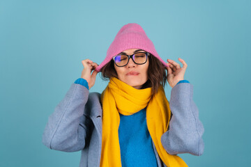 Spring autumn portrait of a woman in a blue knitted sweater, glasses, a yellow bright scarf and a gray coat, smiling cheerfully, posing fashionably, in pink hat