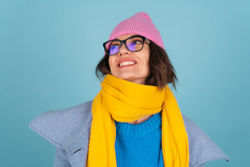 Spring autumn portrait of a woman in a blue knitted sweater, glasses, a yellow bright scarf and a gray coat, smiling cheerfully, posing fashionably, in pink hat