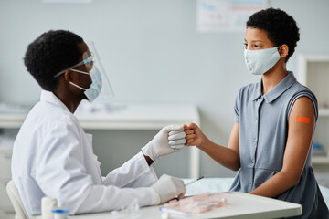 Obraz premium Portrait of teenage African-American girl bumping fists with doctor after getting vaccinated against covid-19
