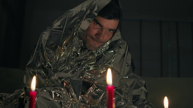 Man suffers from electromagnetic hypersensitivity and hides under a metal blanket in dark room with candles. Electromagnetic hypersensitivity EHS or allergy to electricity