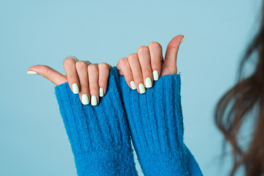 Close shot of a woman's hand in a blue knitted sweater with a large bulky green rhinestone ring and mint spring perfect manicure gel polish on nails