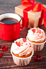 Valentines cupcakes cream cheese frosting decorated with heart candy, mug of coffee and gift box on the wooden background.