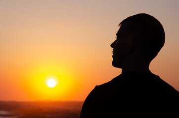 Silhouette of man against sunset sky. Person stands with his back against background of yellow sky with copy space. Male admires sunrise and thinks about future.