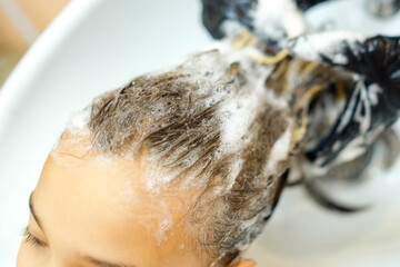 Naklejka premium The girl is washed her hair in the salon. Shampoo bubbles close up
