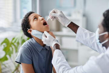 African-American of doctor dropping liquid in mouth of child during oral vaccination in clinic - obrazy, fototapety, plakaty