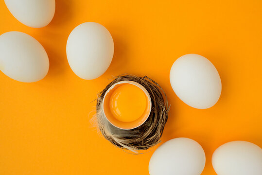White eggs and egg yolk into nest on yellow background. Top view. Flat lay. Easter celebration