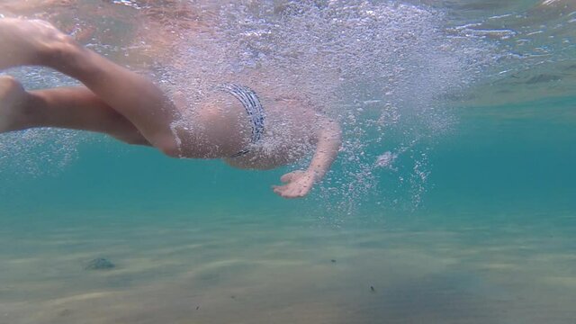 A child in an underwater mask learns to swim and dive. The boy dives into the sea.