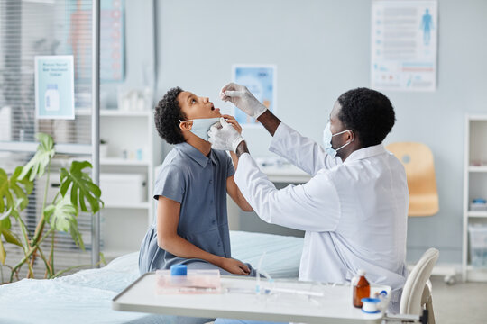 Side view portrait of African-American of doctor dropping liquid in mouth of child during oral vaccination in clinic