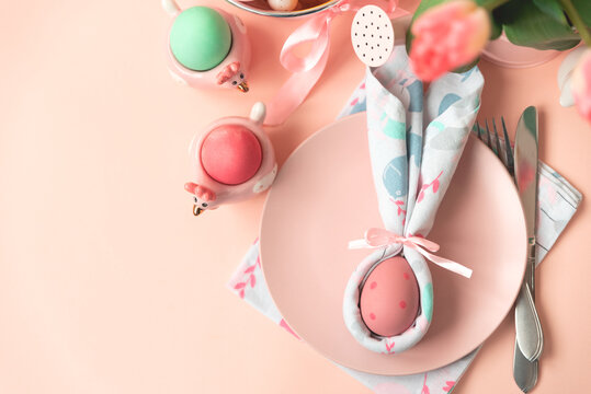 Festive Easter table setting with napkin Easter Bunny on pink table. Easter celebration concept. Soft focus. Top view. Copy space