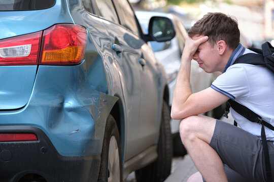 Stressed man driver sitting on street side shocked after car accident. Road safety and insurance concept