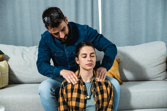 Young couple in love a woman sitting on the floor and a guy on the couch and gently massages her shoulders and head to relax her muscles after a hard day at work and to relieve her of stress.