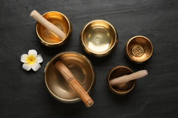 Golden singing bowls, mallets and flower on black table, flat lay