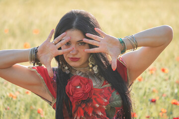 Gypsy girl in a field of poppies. Red gypsy dress. Beautiful brunette woman in nature. - obrazy, fototapety, plakaty