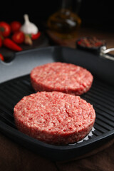 Raw hamburger patties with oil on grill pan, closeup
