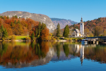 Fototapeta na wymiar Heartwarming view of lake Bohinj in vibrant autumnal colors and catholic church