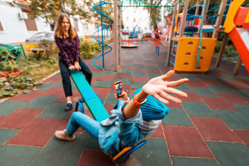 Two childish happy woman friends or teenage girl having fun on seesaw on a playground. Concept of...