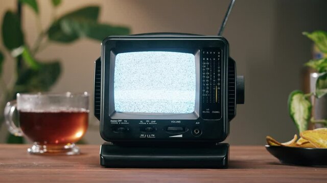 Small old television with grey interference screen on home background. Close-up of vintage tv on table with hot tea, nostalgia. 