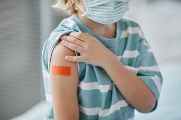 Close up of little boy showing shoulder patch after getting vaccinated against covid 19 in clinic,...