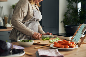 Unrecognizable caucasian senior woman cutting vegetables while cooking in the kitchen