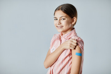 Obraz premium Portrait of cute girl showing shoulder patch and smiling at camera after getting vaccinated, copy space