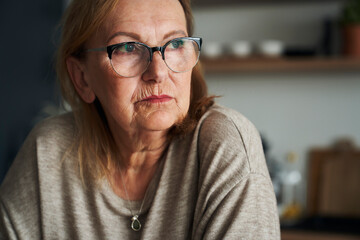 Thoughtful caucasian senior woman sitting in the kitchen and looking away