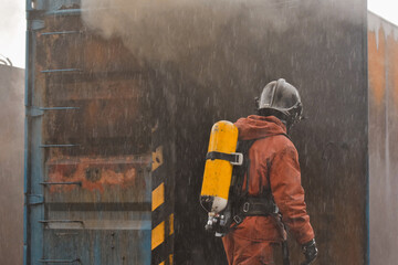 Hombre vestido de bombero a punto de entrar en una instalación incendiada durante una tormenta - obrazy, fototapety, plakaty