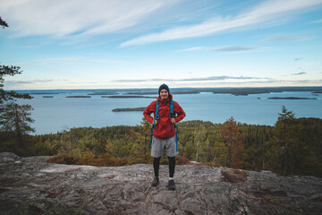 Fototapeta premium Laughing backpacker standing on a rock with Lake Jatkonjarvi behind him in Koli National Park, eastern Finland. The man, aged 24, smiles naturally. Active lifestyle
