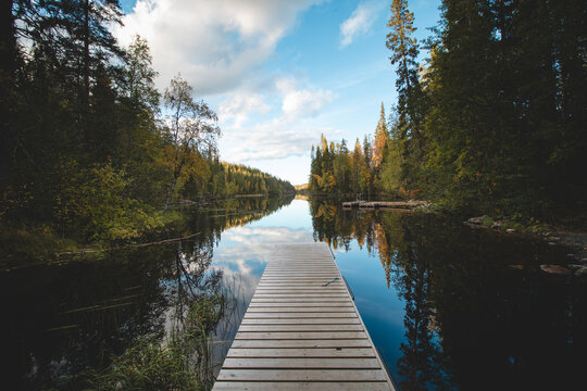 View of a wooden pier and a still river reflecting the colourful autumn forest with all its colours. Wonderful autumn in the barren wilderness of Hossa National Park, in Lapland, northern Finland