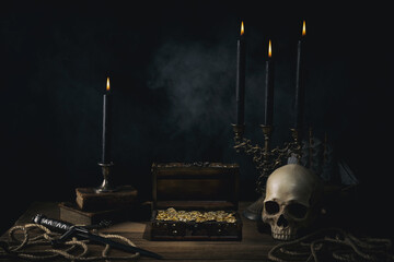Treasure chest with a gold coins,dagger and human skull on a pirate captain table in the light of...