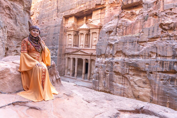 woman dressed in traditional clothes and headscarf staying at the top of rock on the background is...