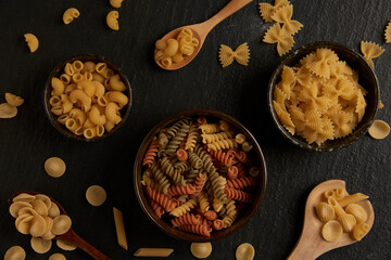 pasta concept some of various kinds of pasta put into a small bowl, some put on a wooden spoon, and some put on the dark background