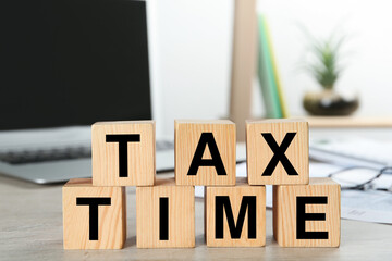 Wooden cubes with words Tax Time near laptop on table indoors