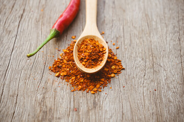 ground dried chillies in wooden spoon with fresh red chilli on wood background
