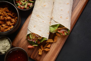 Shawarma Rolled Sandwich with Sauce and vegetables, Arab Traditional Food. Shawarma Doner kebab wrap with chicken, fries and pickles. Israeli Traditional homemade Shawarma on wooden cutting board.