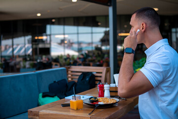 Young handsome businessman eating in a restaurant while using airpods