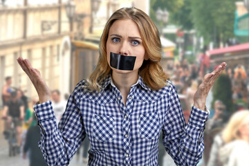 Female protestor with black tape over her mouth demonstrating protest standing outdoors.