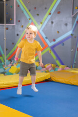 Fototapeta na wymiar cute blond little boy jumps in a trampoline park, children activity