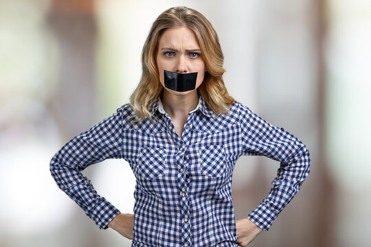 Irritated angry young woman with mouth covered with tape.
