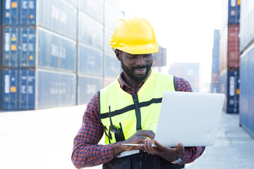 Portrait Black American African warehouse staff wearing yellow hard hat, construction vest and ear protector standing with happy smile and checking list of container boxes for shipping logistic stock.