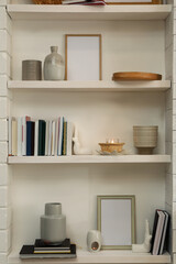 Books, empty frames and different decor on shelves indoors. Interior design