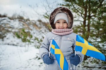 Scandinavian baby girl with Sweden flag in winter swedish landscape.